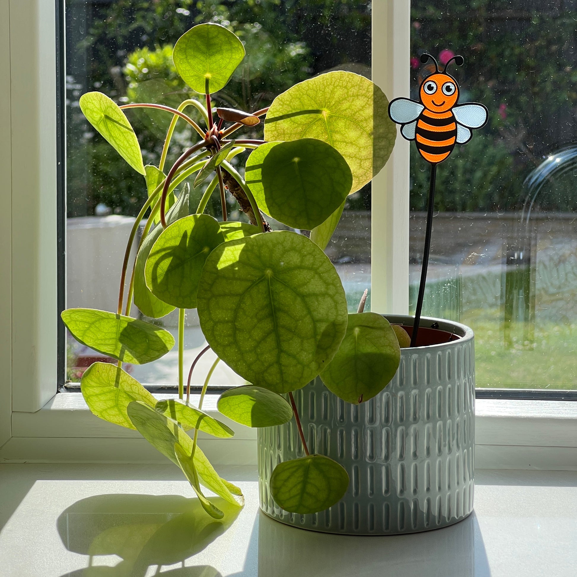 Bee decorative stem displayed in a houseplant pot beside a sunny window.