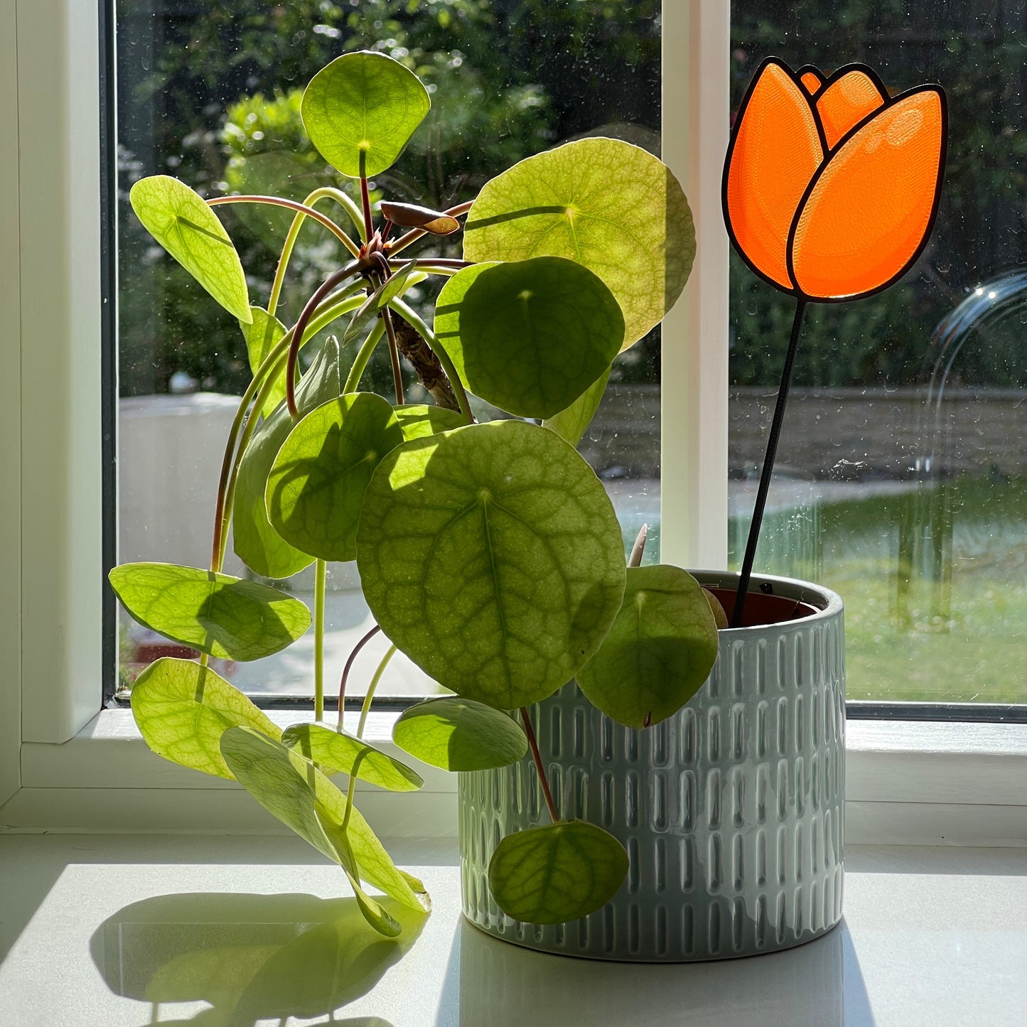 Orange tulip decorative stem displayed in a houseplant pot beside a sunny window.