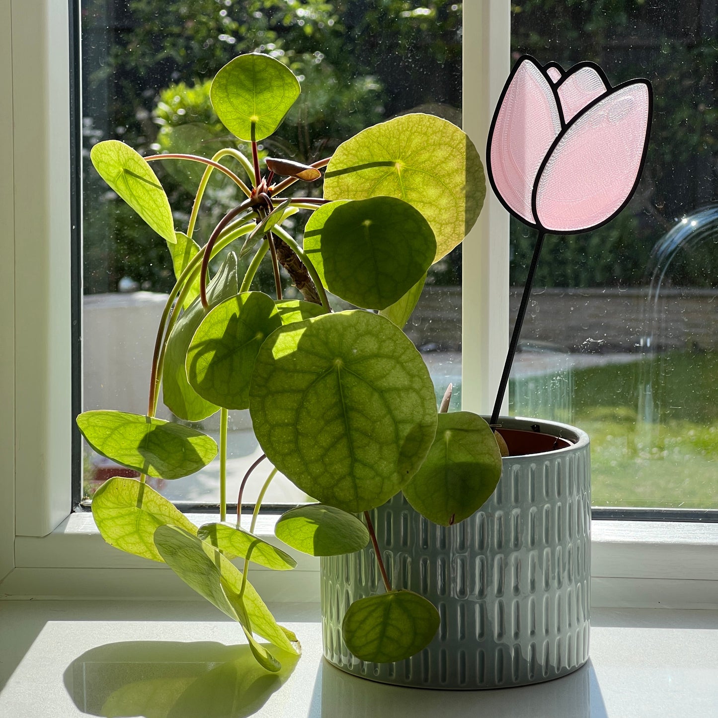 Pink tulip decorative stem displayed in a houseplant pot beside a sunny window.