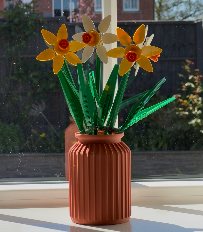 Vase with artificial flowers on a windowsill with a house in the background