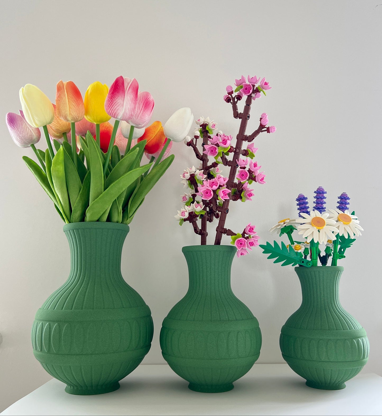 Three green vases with flowers on a white surface against a light gray background