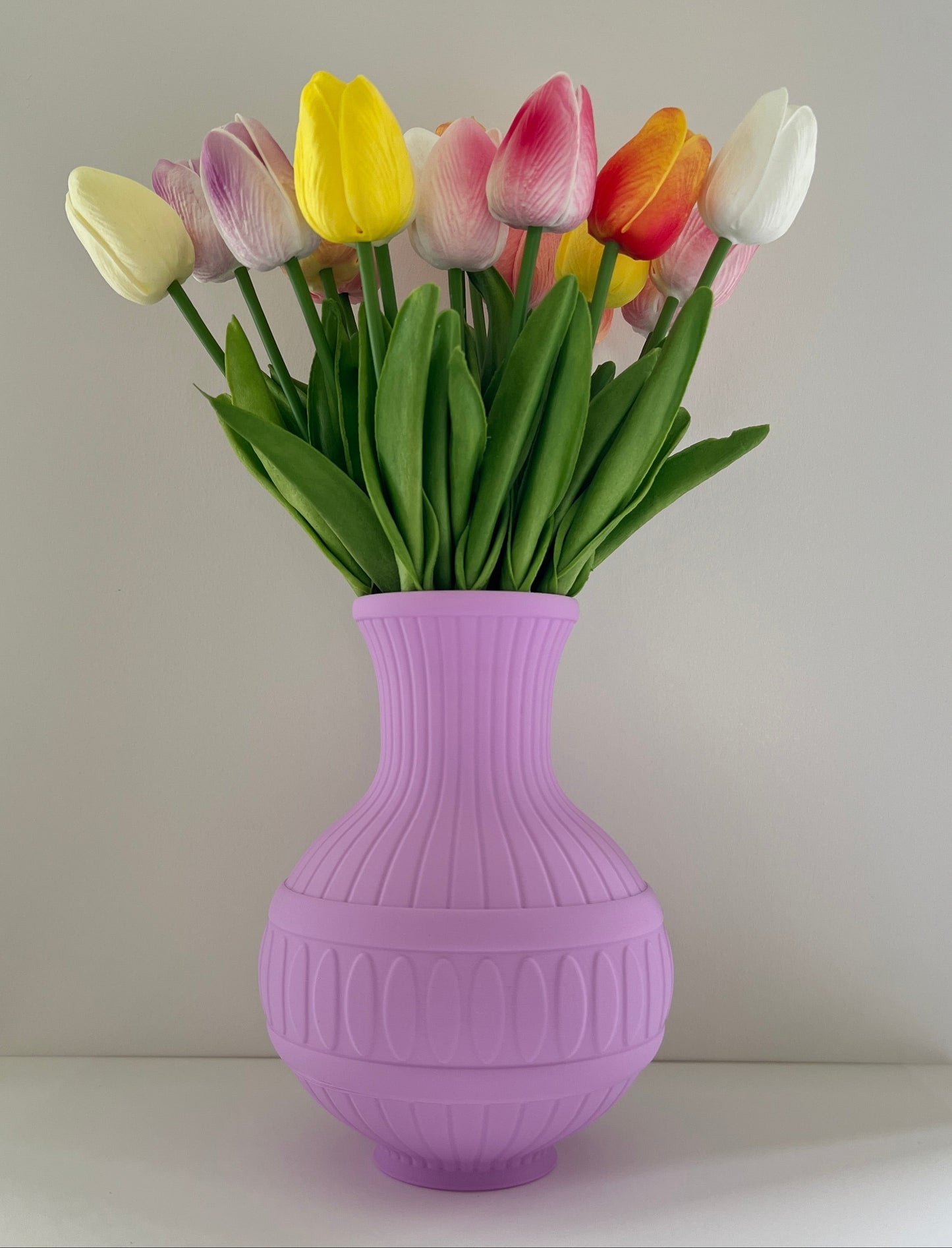Purple vase with colorful tulips on a white surface against a light gray background