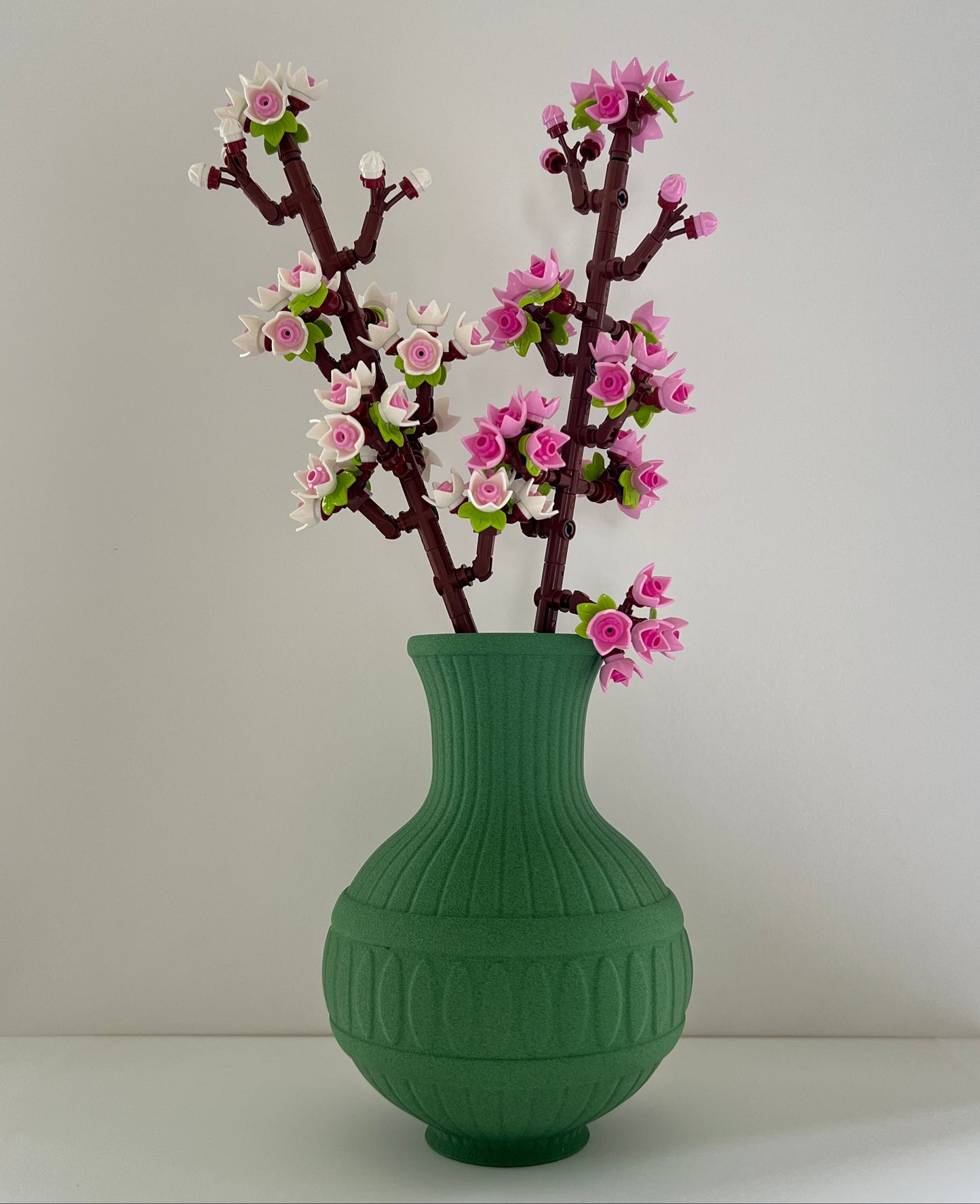 Green vase with decorative branches and pink flowers on a plain background