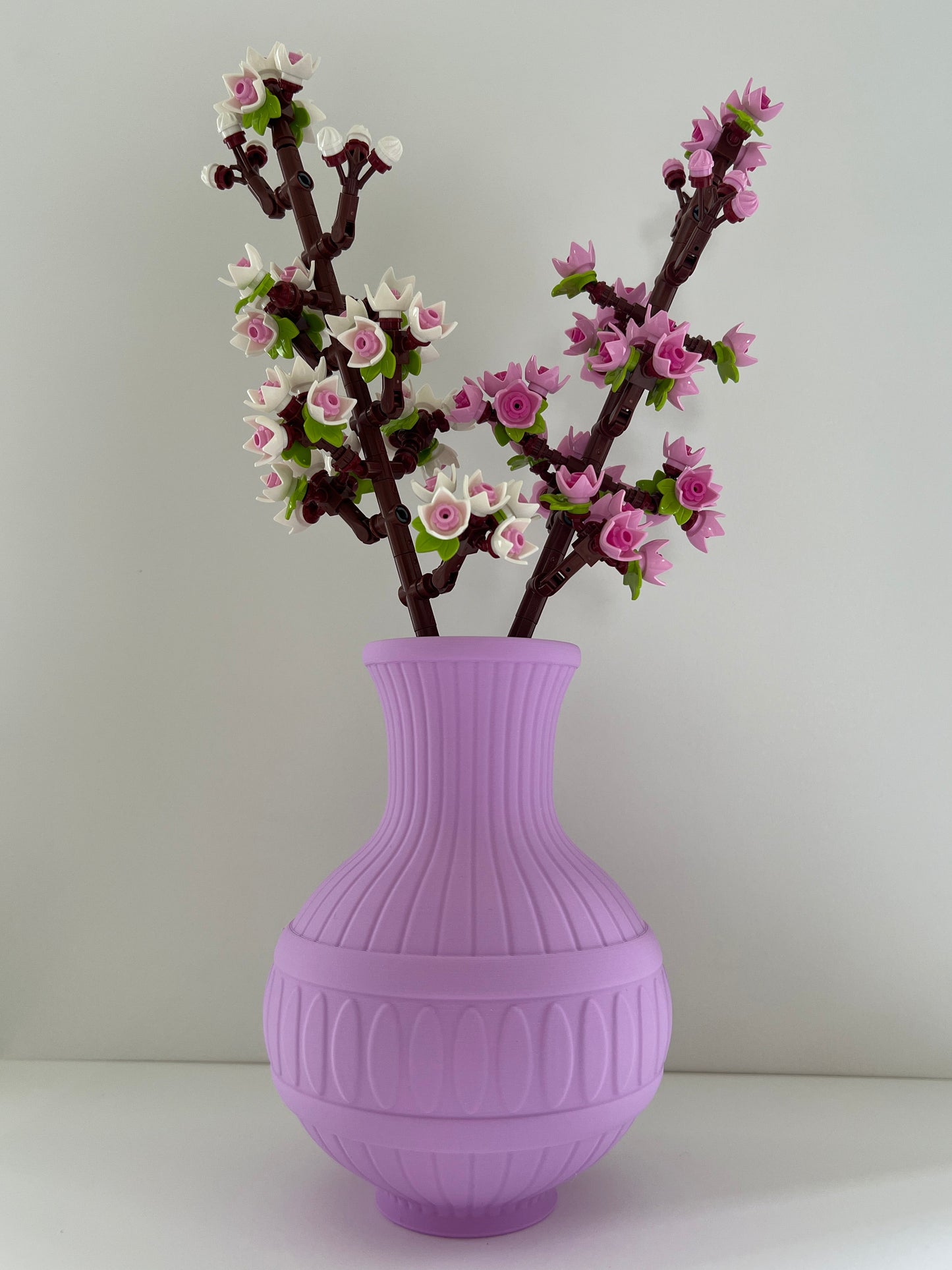 Purple vase with decorative branch and flowers on a light gray background