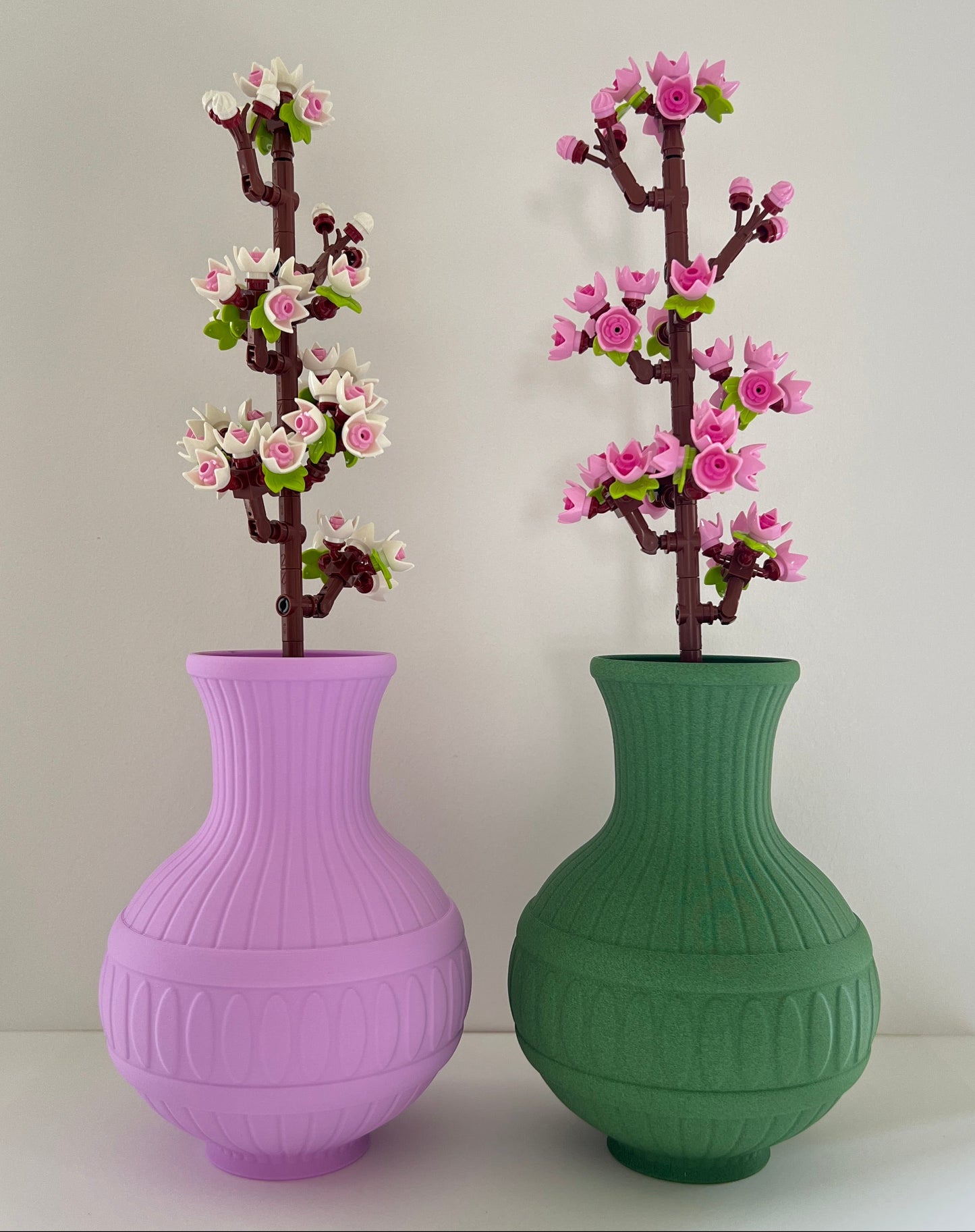Two decorative vases, one purple and one green, with floral branches on a white surface.