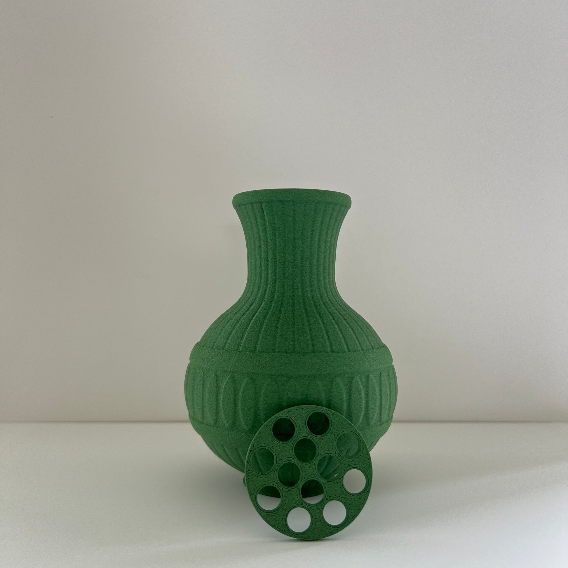 Green vase with decorative branches and pink flowers on a plain background
