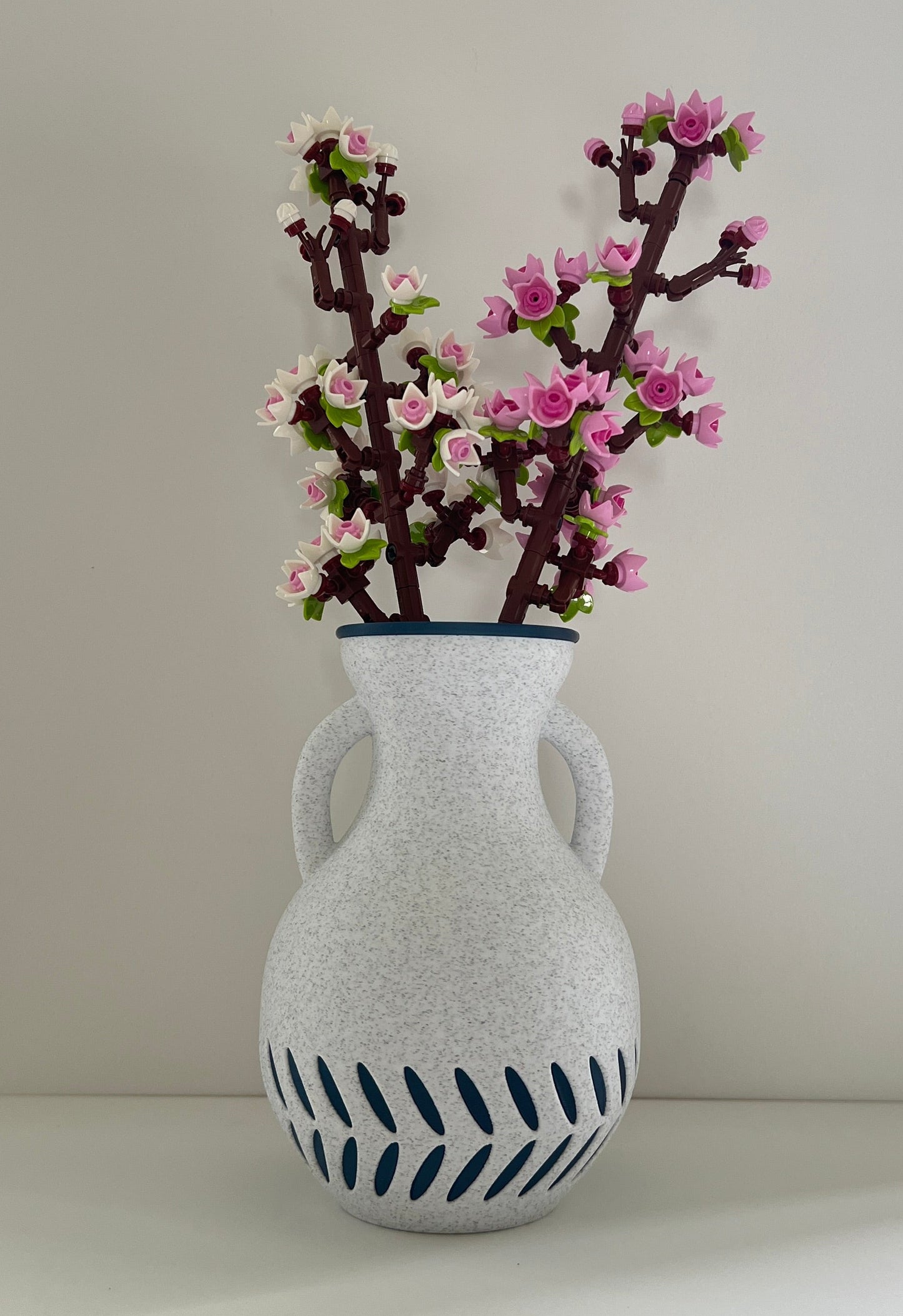 White textured vase with blue patterns holding pink flowers on a white surface.