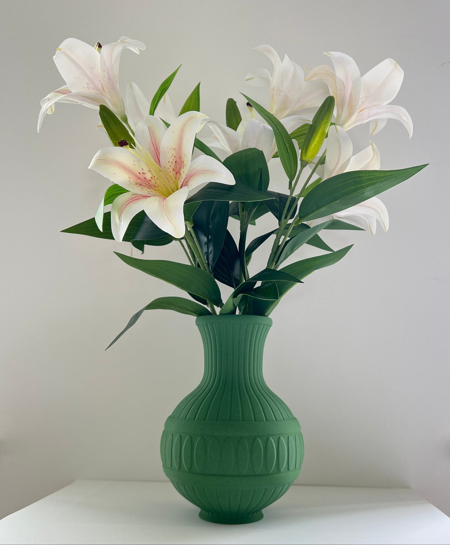 Green vase with white flowers on a white surface against a light gray background